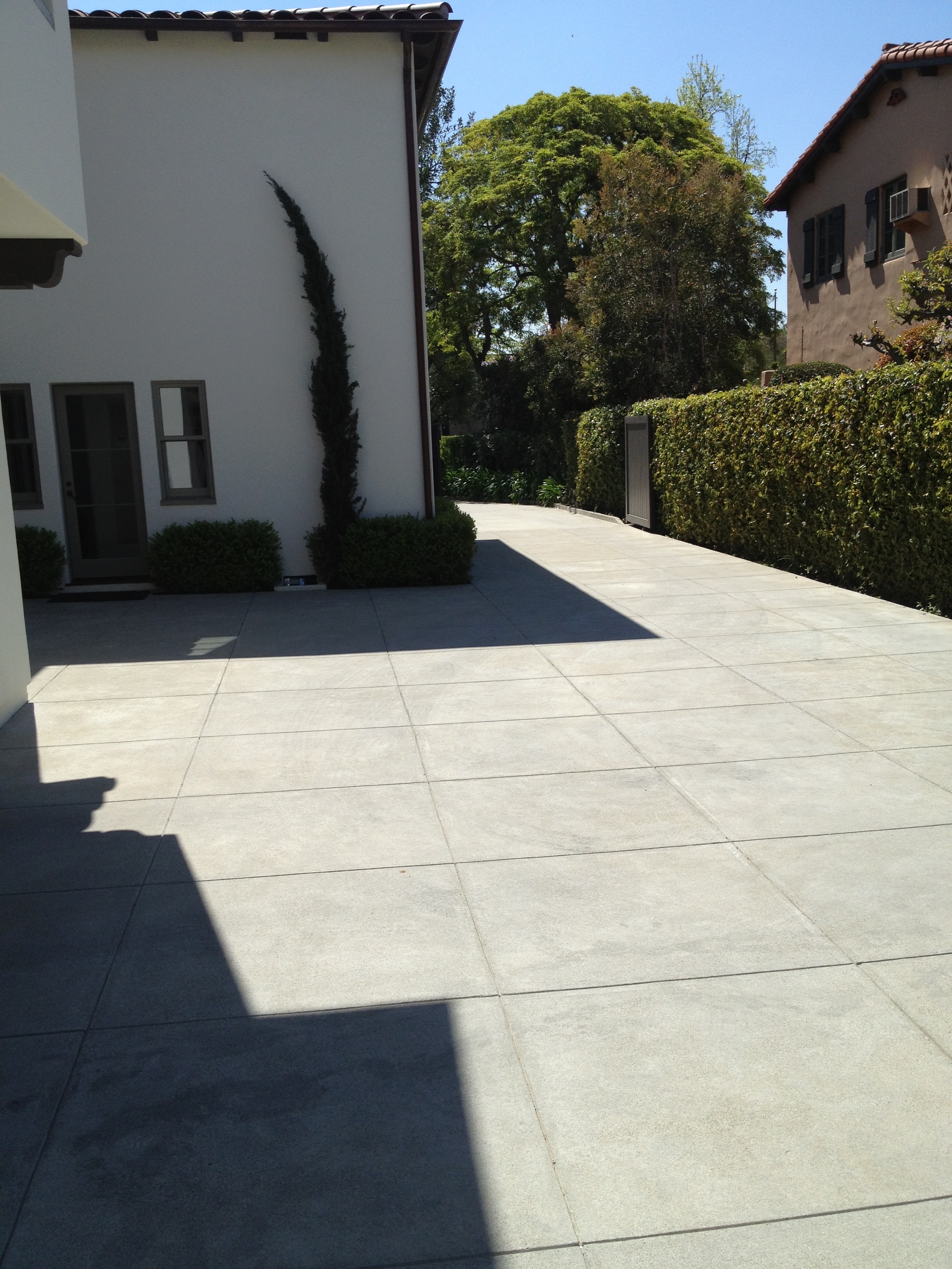 Wide sand finish concrete driveway with large score line grid pattern at a Spanish-style home in Pasadena, surrounded by mature trees and ivy-covered walls by Concrete Etc., Inc.