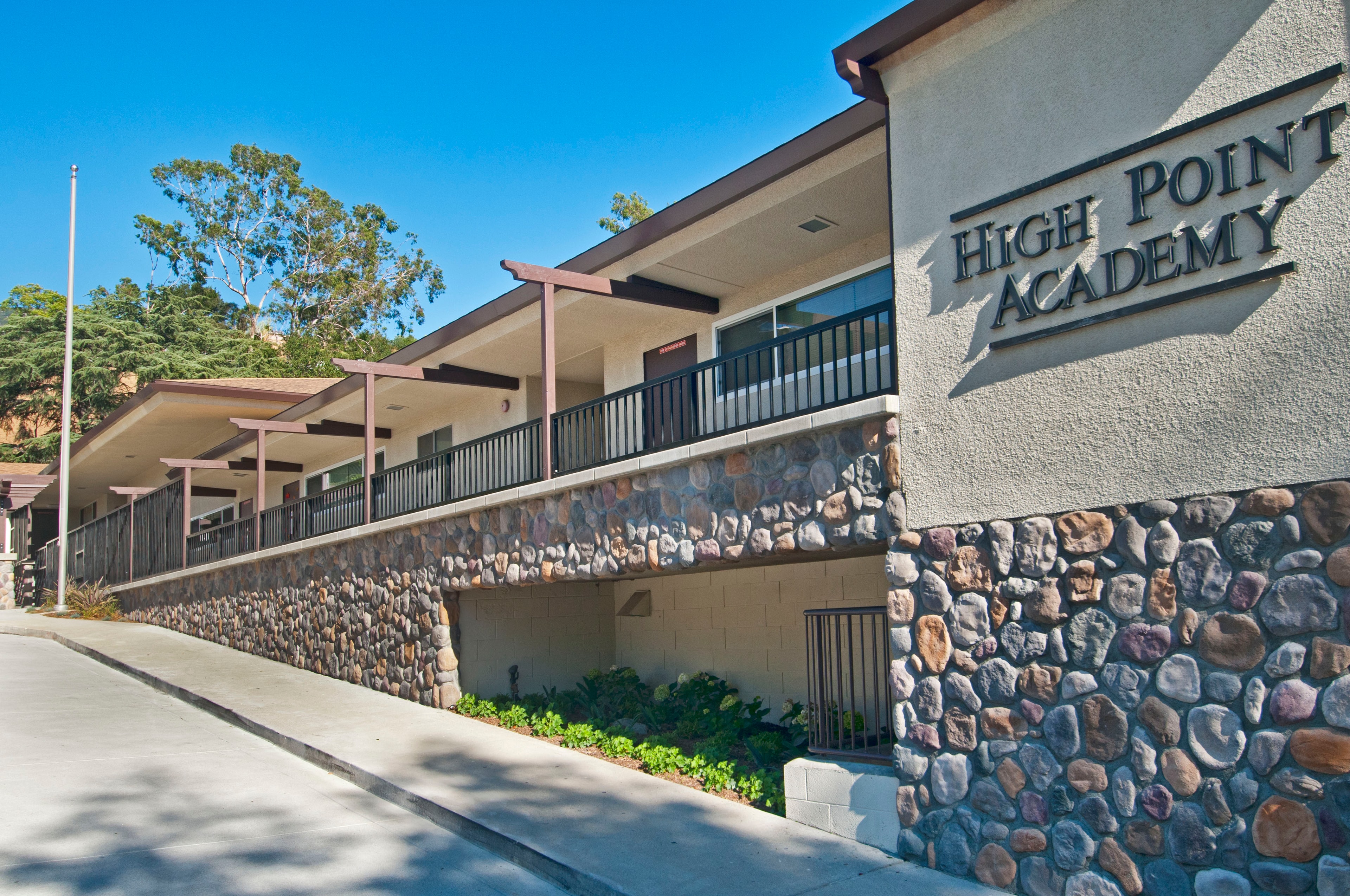 Building exterior with river rock stone veneer retaining wall and concrete walkway — Concrete Etc., Inc.